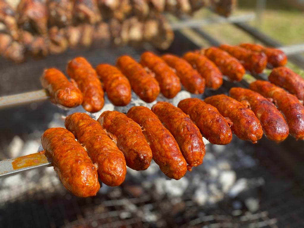 Multiple skewers with sausages grilling over hot charcoal outdoors.