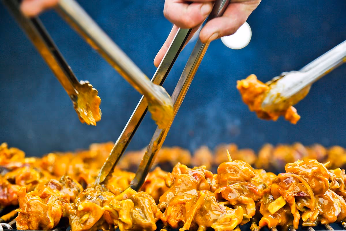 Close-up of grilling venison sosaties being turned with tongs over hot coals.