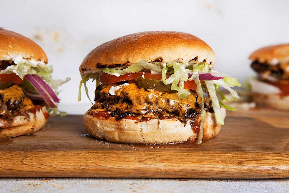 Grilled cheeseburger with lettuce, tomato, pickles, and red onion on a wooden board.