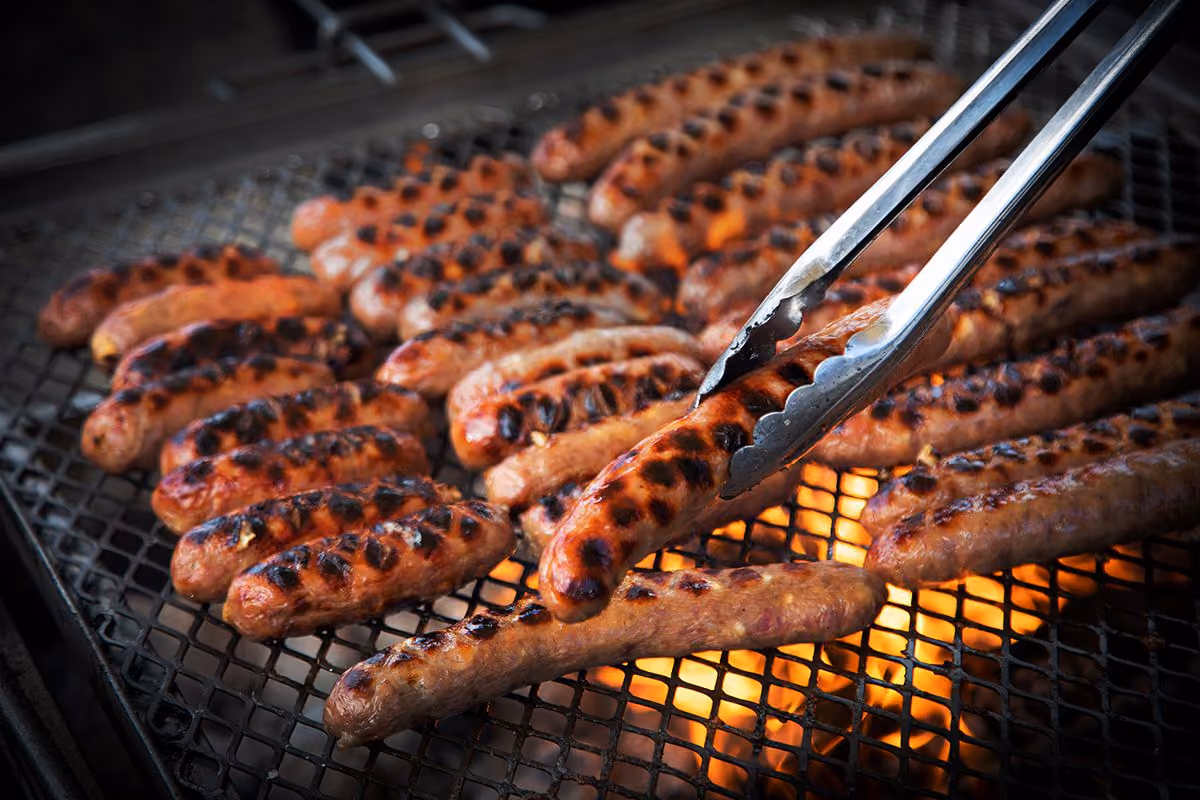Rows of grilled sausages on metal skewers over hot coals.
