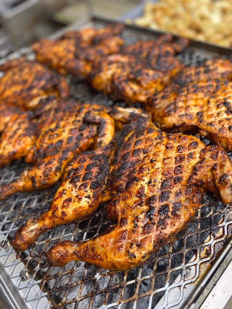 Multiple grilled chicken halves with char marks laid out on a metal grill grate.
