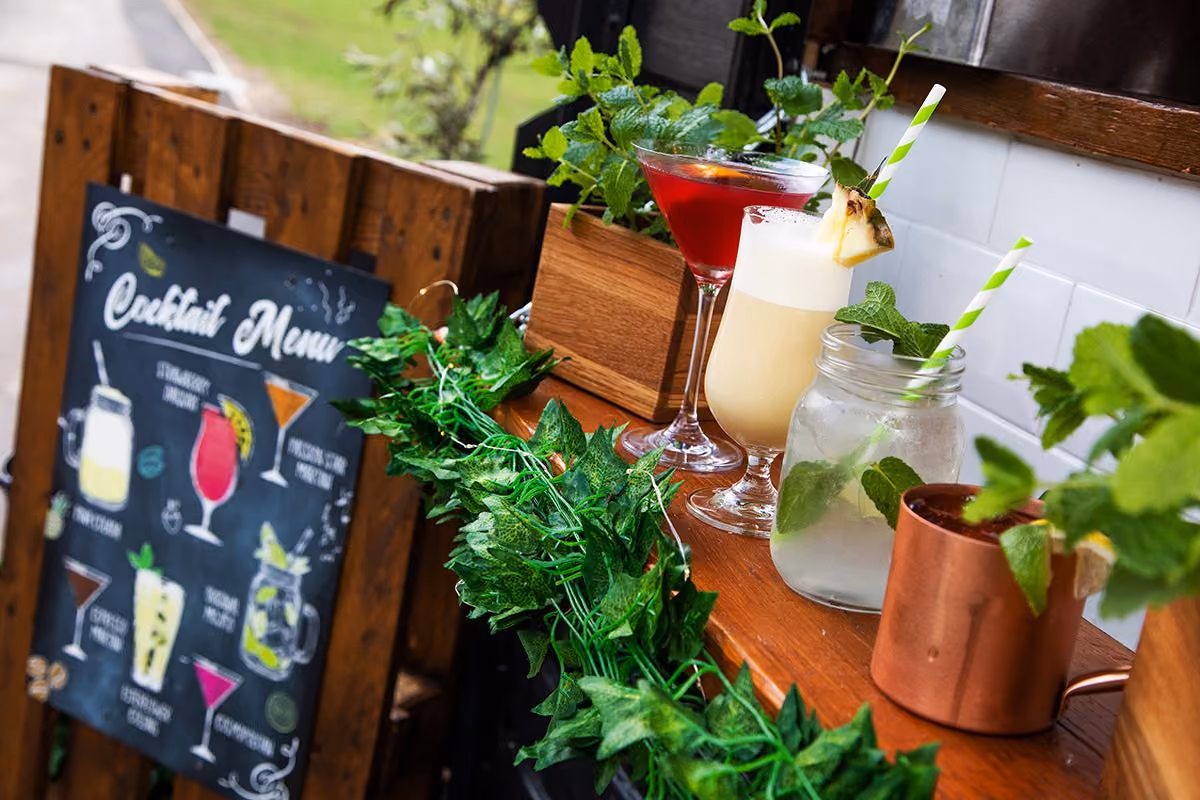 A wooden bar with four colourful cocktails garnished with mint and pineapple, next to a cocktail menu.
