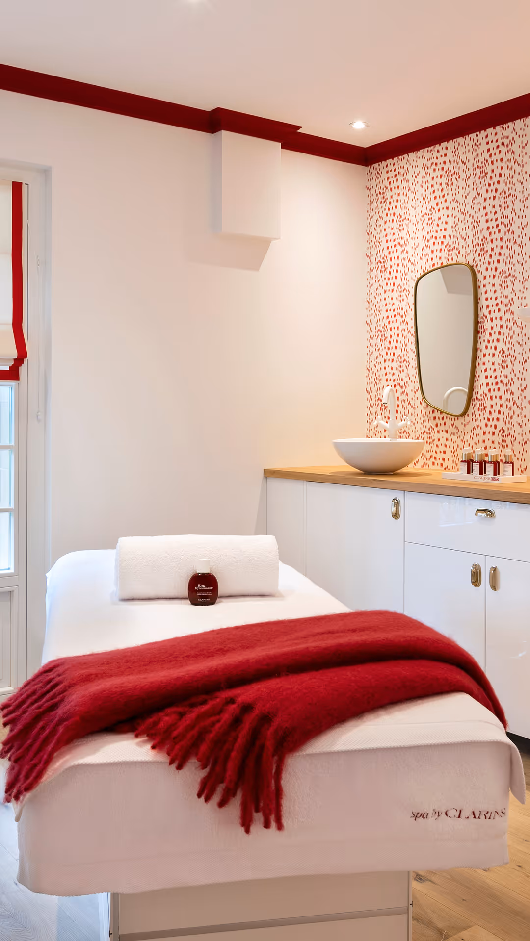 Massage table with a white towel and a red blanket in a bright spa room.