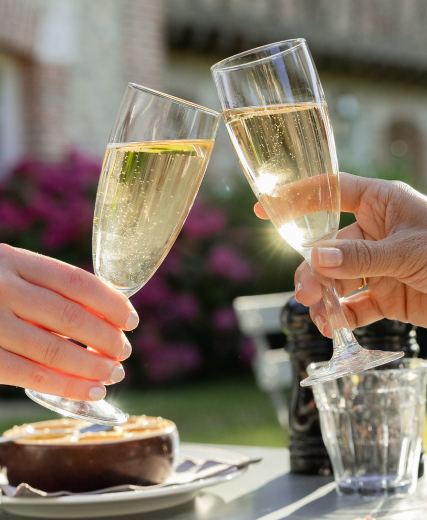 Two hands toast with sparkling champagne flutes outside in the sun.