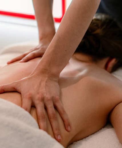 Two hands apply a deep massage to the bare back of a person lying on a table.