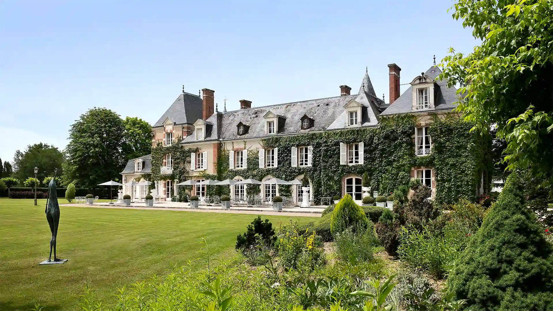 Facade of a large manor house covered in ivy with a manicured garden and a statue in the lawn, Les Hauts de Loire, 5-star luxury hotel in Veuzain-sur-Loire, Loire Valley, France.