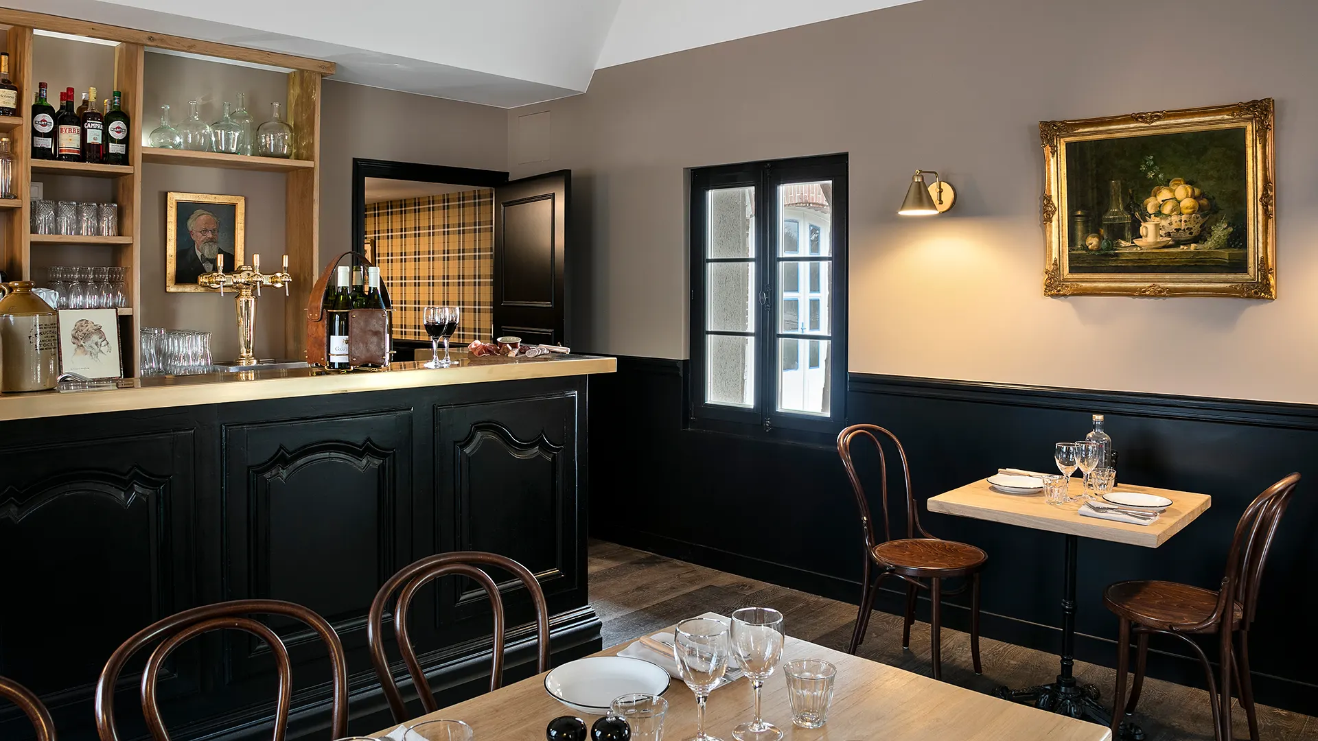 Interior of an elegant bar with wooden counter, curved wooden chairs and paintings hanging on the walls.