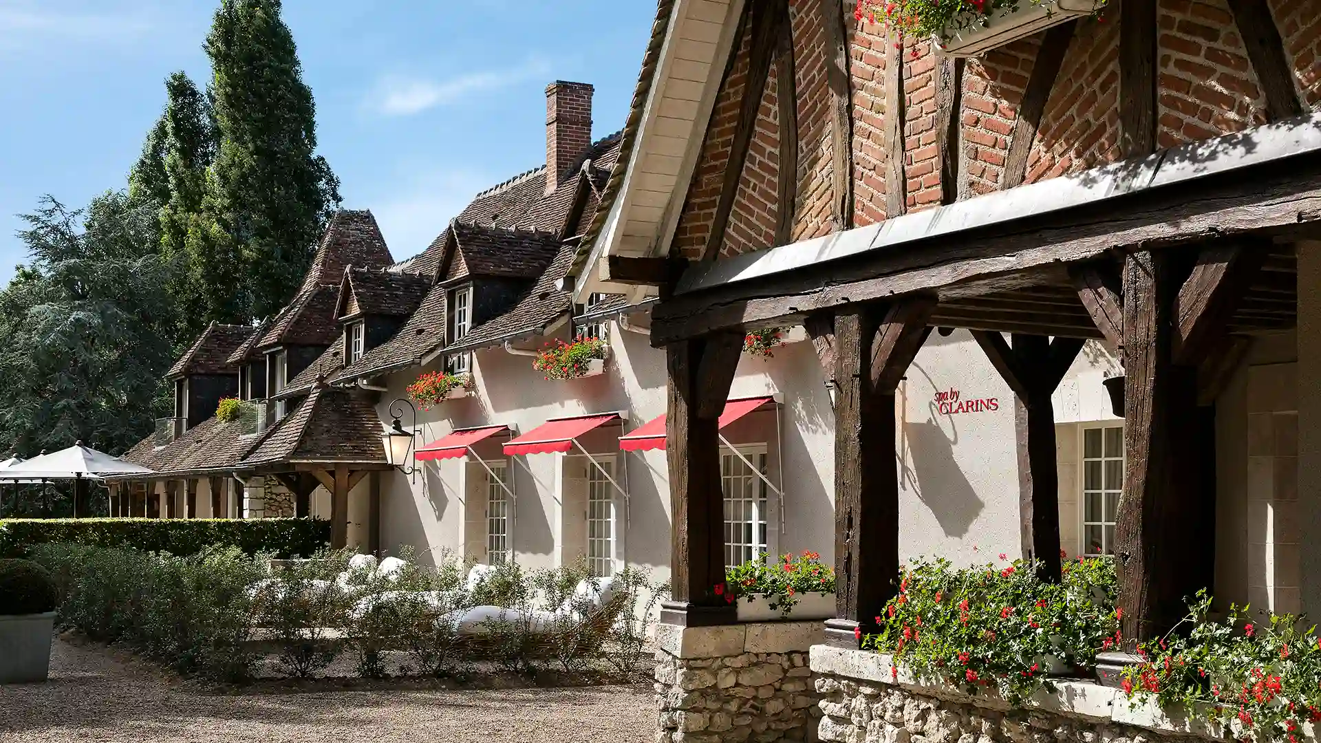Facade of a stone house with tiled roofs, flower planters and red awning.