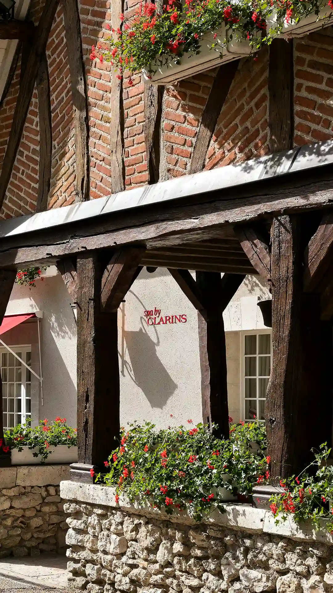 Facade of a half-timbered building with red flowers and the text spa by CLARINS on a white wall.