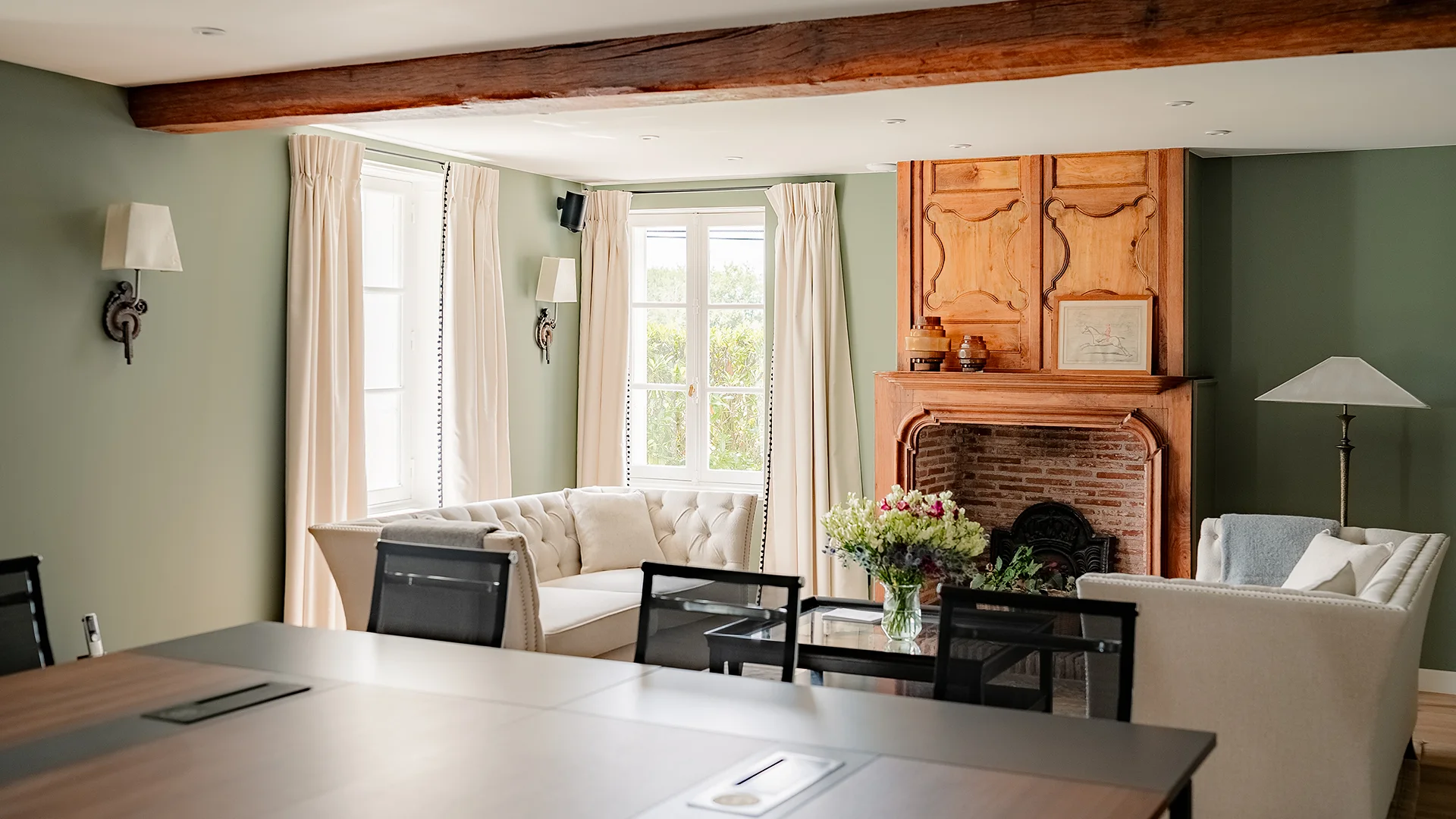 Helles Wohnzimmer mit cremefarbenen Sofas, Holzkamin, großem Tisch und Wandlampen.