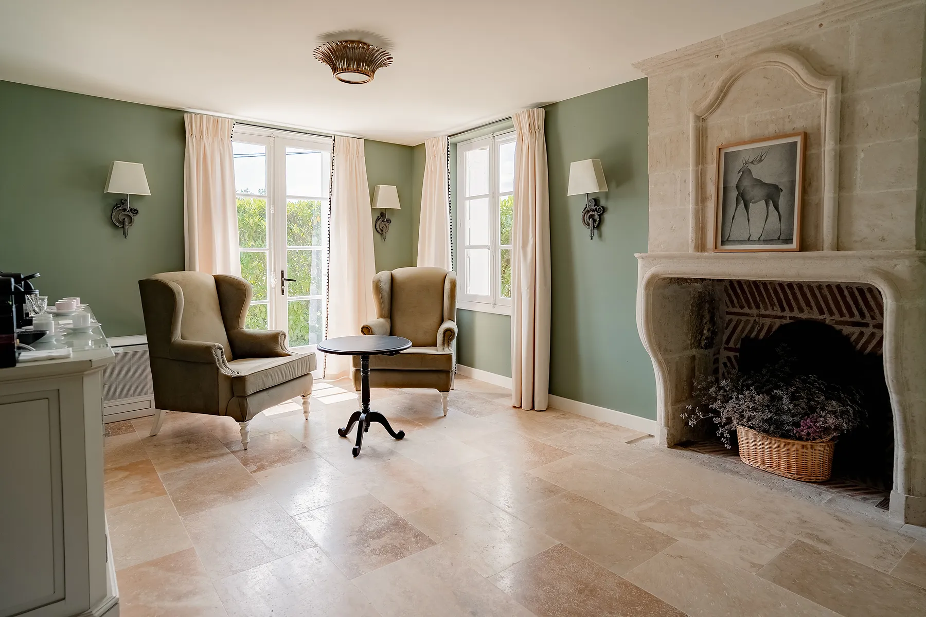 Salon avec fauteuils verts, table ronde noire, cheminée en pierre et murs verts clairs, Les Hauts de Loire, hôtel de luxe 5 étoiles à Veuzain-sur-Loire, Vallée de la Loire, France.
