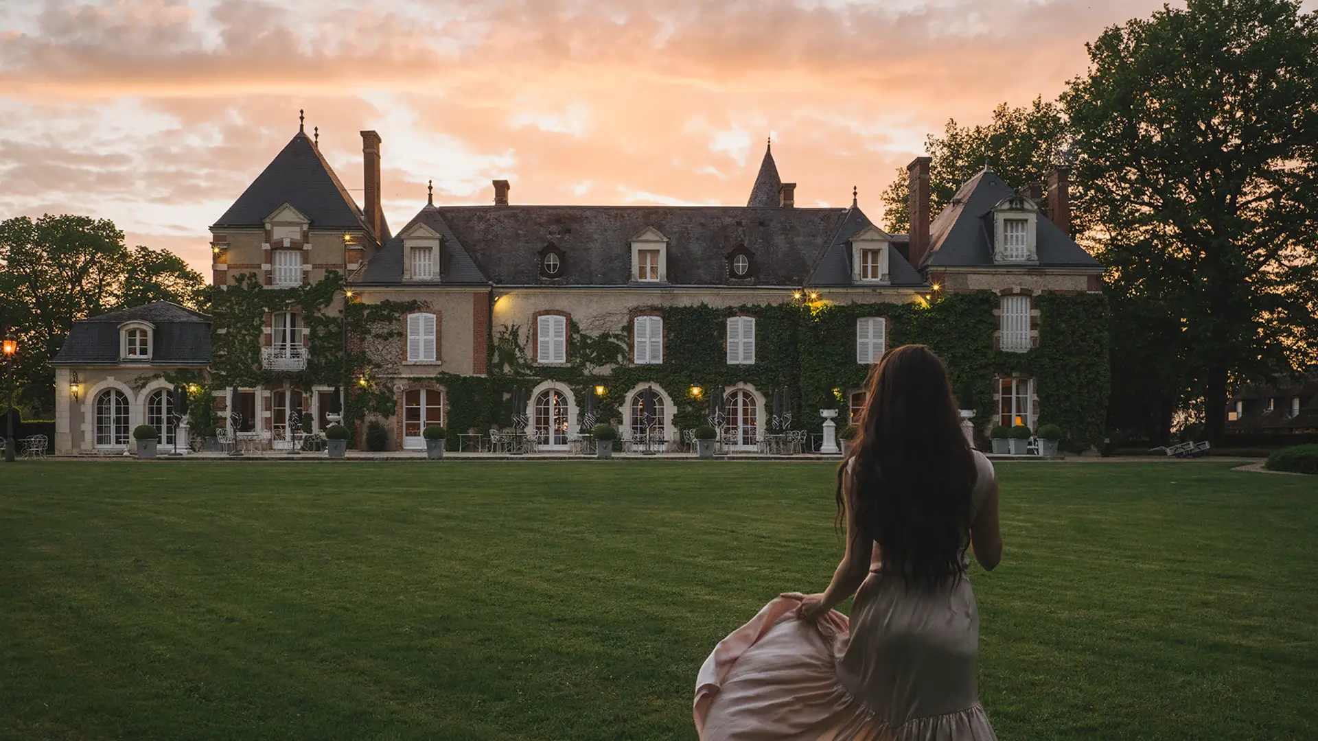 Les Hauts de Loire — Hotel, Restaurant & Spa — 5 stars: woman in a pink dress watching a mansion covered in ivy at sunset.
