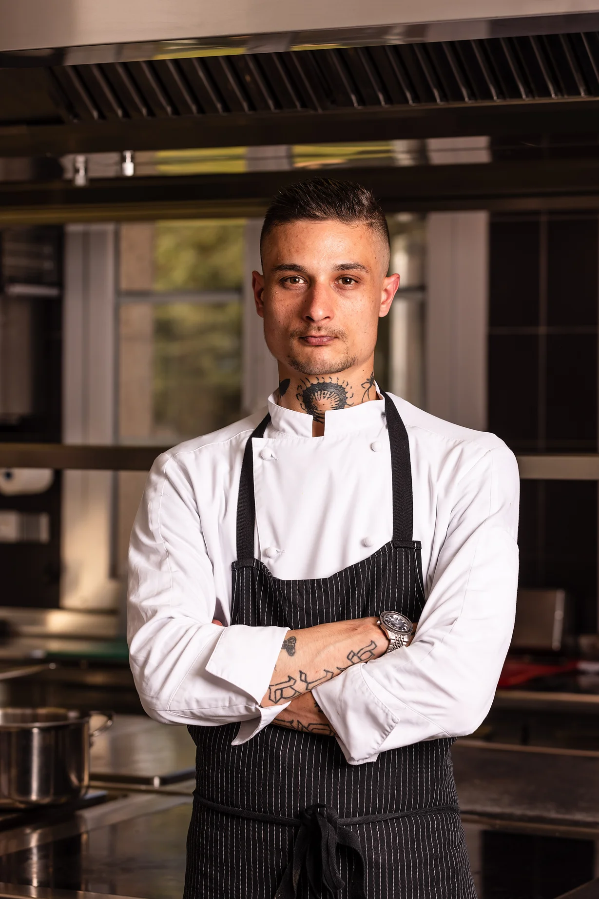 Chef Arthur-Peta, with his arms crossed, wears a white chef jacket and a black striped apron in the kitchens of Les Hauts de Loire — Hôtel, Restaurant & Spa — 5 stars.