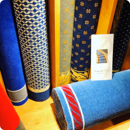 Rouleaux de tapis colorés avec motifs bleu, gris et rouges exposés verticalement et horizontalement.