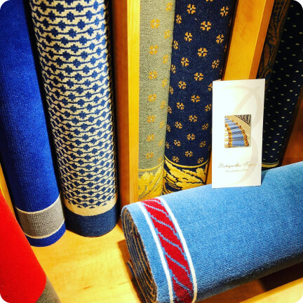Rouleaux de tapis colorés avec motifs bleu, gris et rouges exposés verticalement et horizontalement.