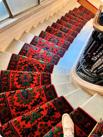 Vue en plongée d'un escalier en marbre avec un tapis rouge à motifs verts et noirs.