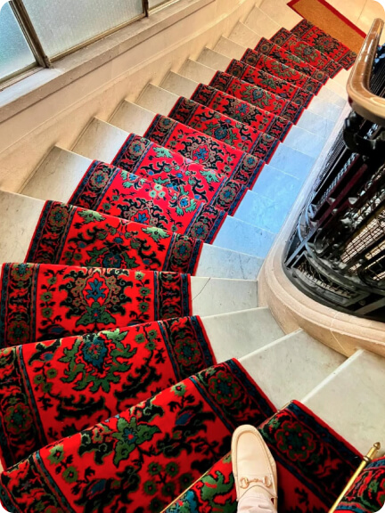 Vue en plongée d'un escalier en marbre avec un tapis rouge à motifs verts et noirs.