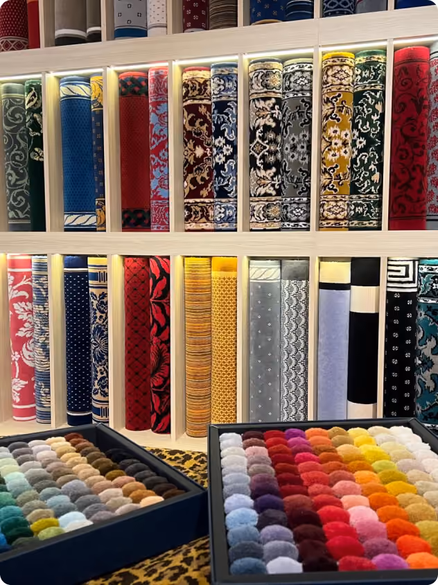 Rouleaux de tapis colorés et échantillons de tissus organisés dans des boîtes sur une table.