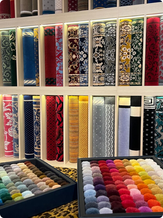 Rouleaux de tapis colorés et échantillons de tissus organisés dans des boîtes sur une table.