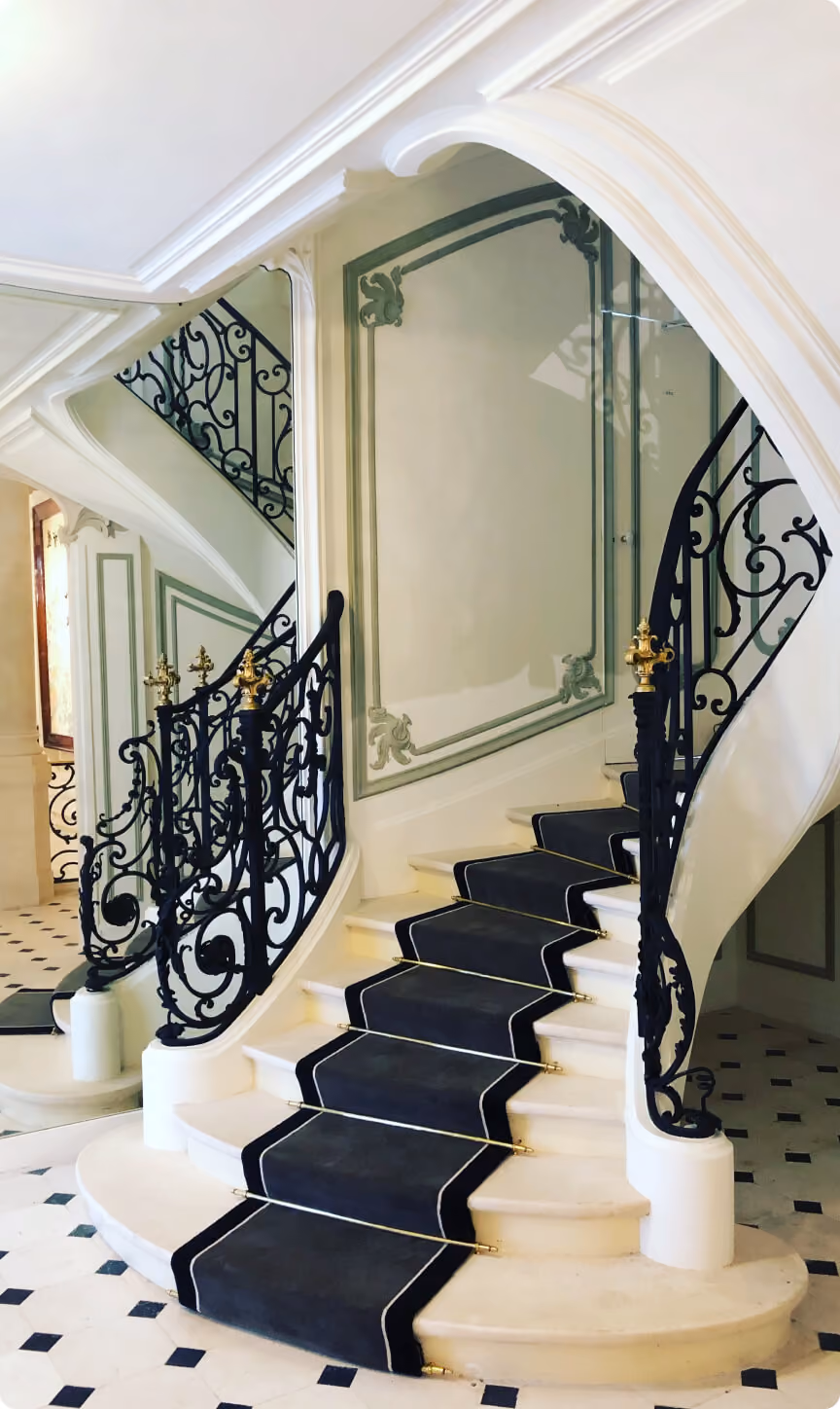 Escalier en marbre avec tapis noir et rampe en fer forgé ornée de décorations dorées.