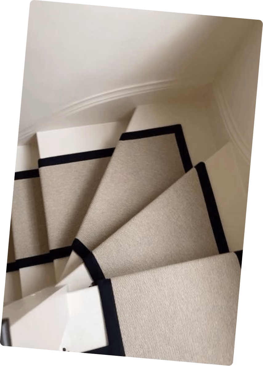 Escalier blanc avec tapis beige bordé de noir descendant en spirale dans un espace étroit.