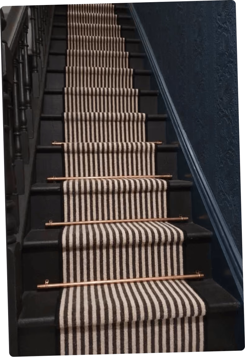 Escalier noir avec un tapis à rayures blanches et noires fixé par des barres métalliques dorées.