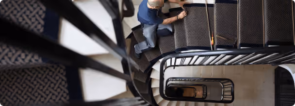 Homme posant un tapis sur un escalier en colimaçon vu de dessus.