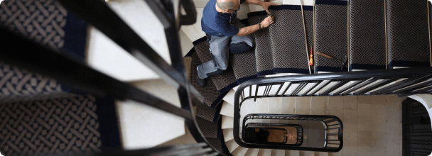 Homme posant un tapis sur un escalier en colimaçon vu de dessus.