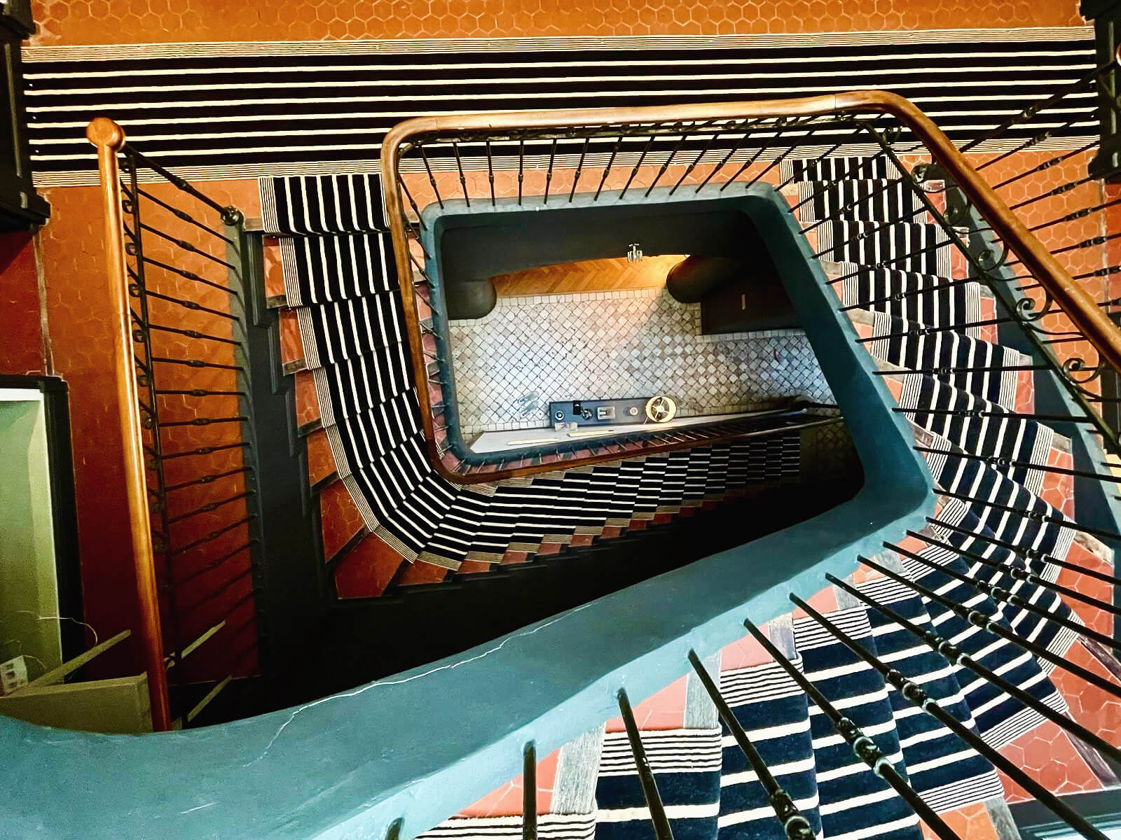 Vue plongeante d'un escalier tournant avec un tapis à rayures noires et blanches.