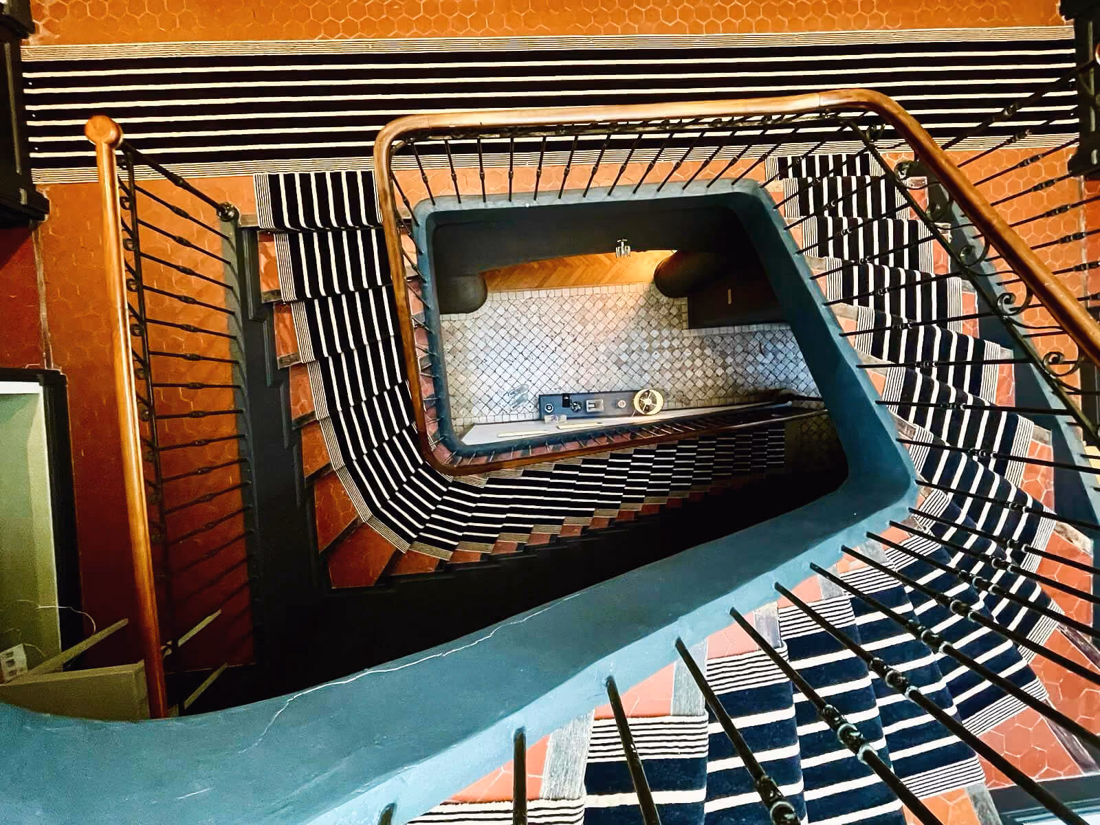 Vue plongeante d'un escalier tournant avec un tapis à rayures noires et blanches.