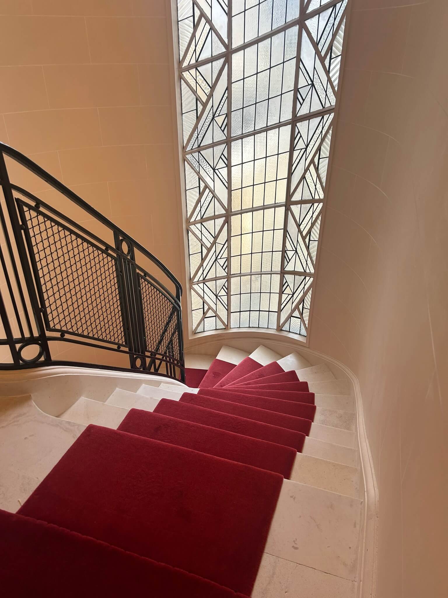 Escalier en colimaçon avec tapis rouge et une grande fenêtre avec motif en verre dépoli.
