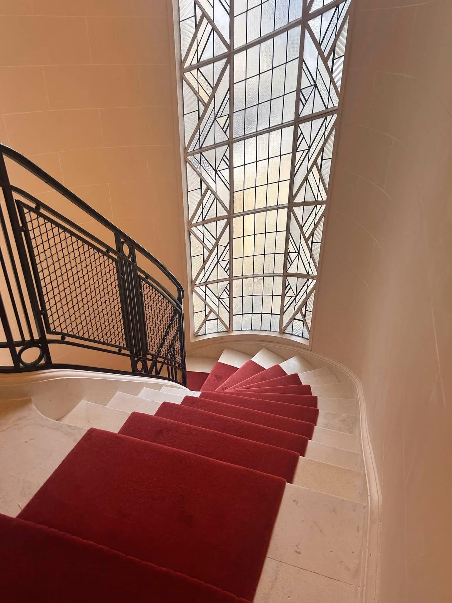 Escalier en colimaçon avec tapis rouge et une grande fenêtre avec motif en verre dépoli.
