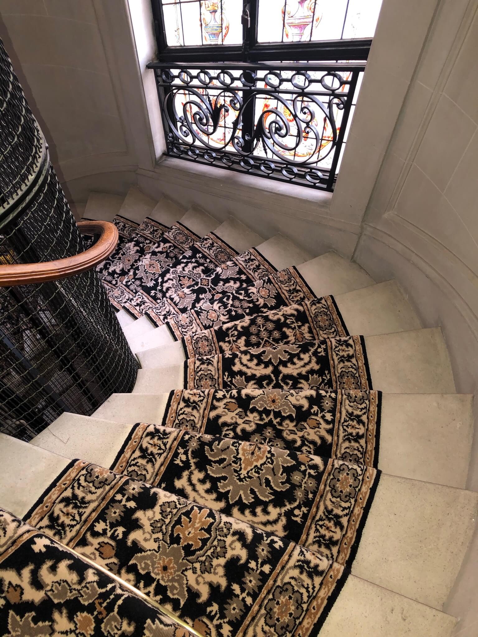Escalier en colimaçon avec un tapis décoratif noir et beige et une rampe en bois.