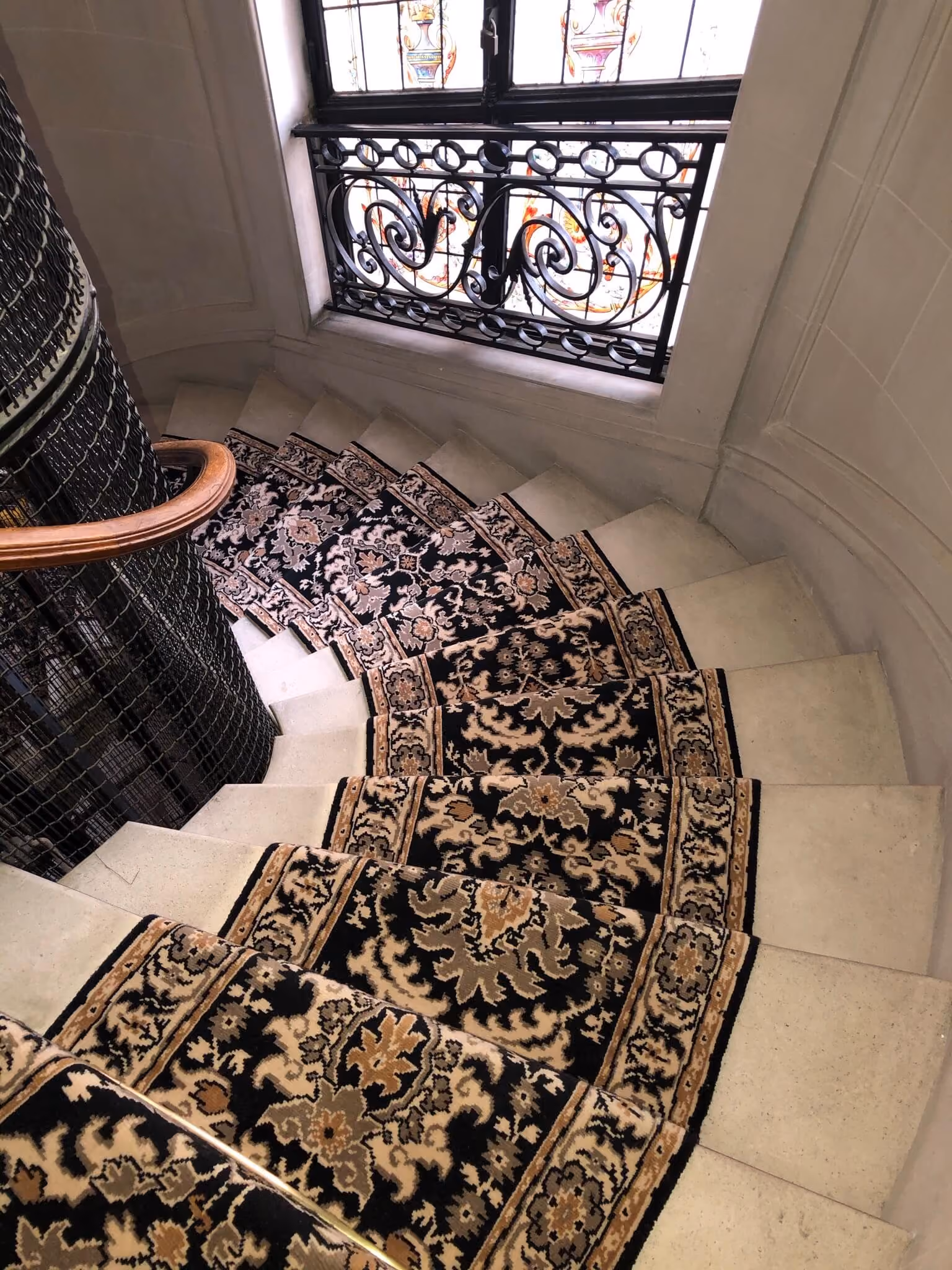 Escalier en colimaçon avec un tapis décoratif noir et beige et une rampe en bois.