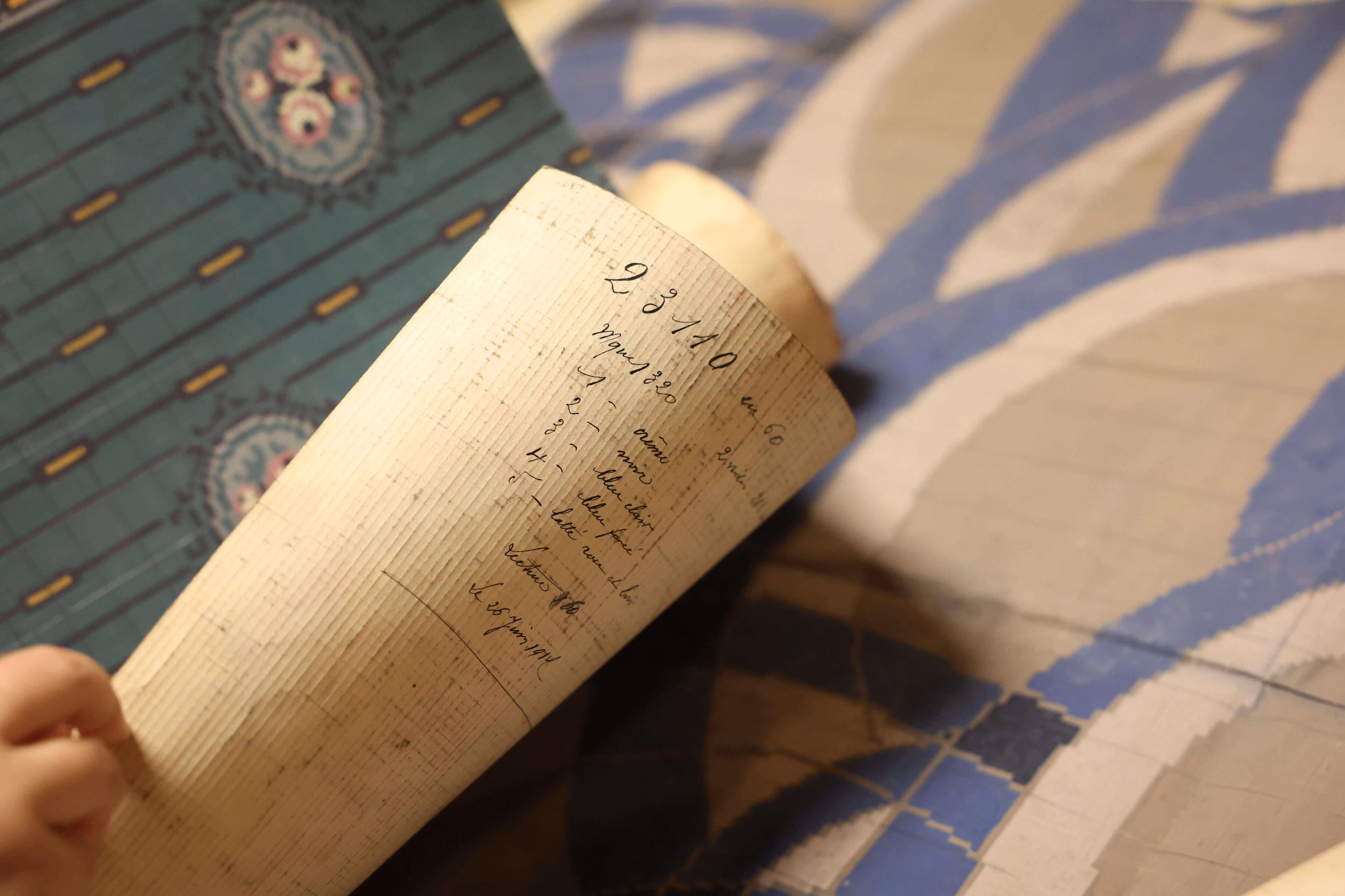 Main de fillette tenant un parchemin avec des mesures manuscrites près d'un sol carrelé à motifs.