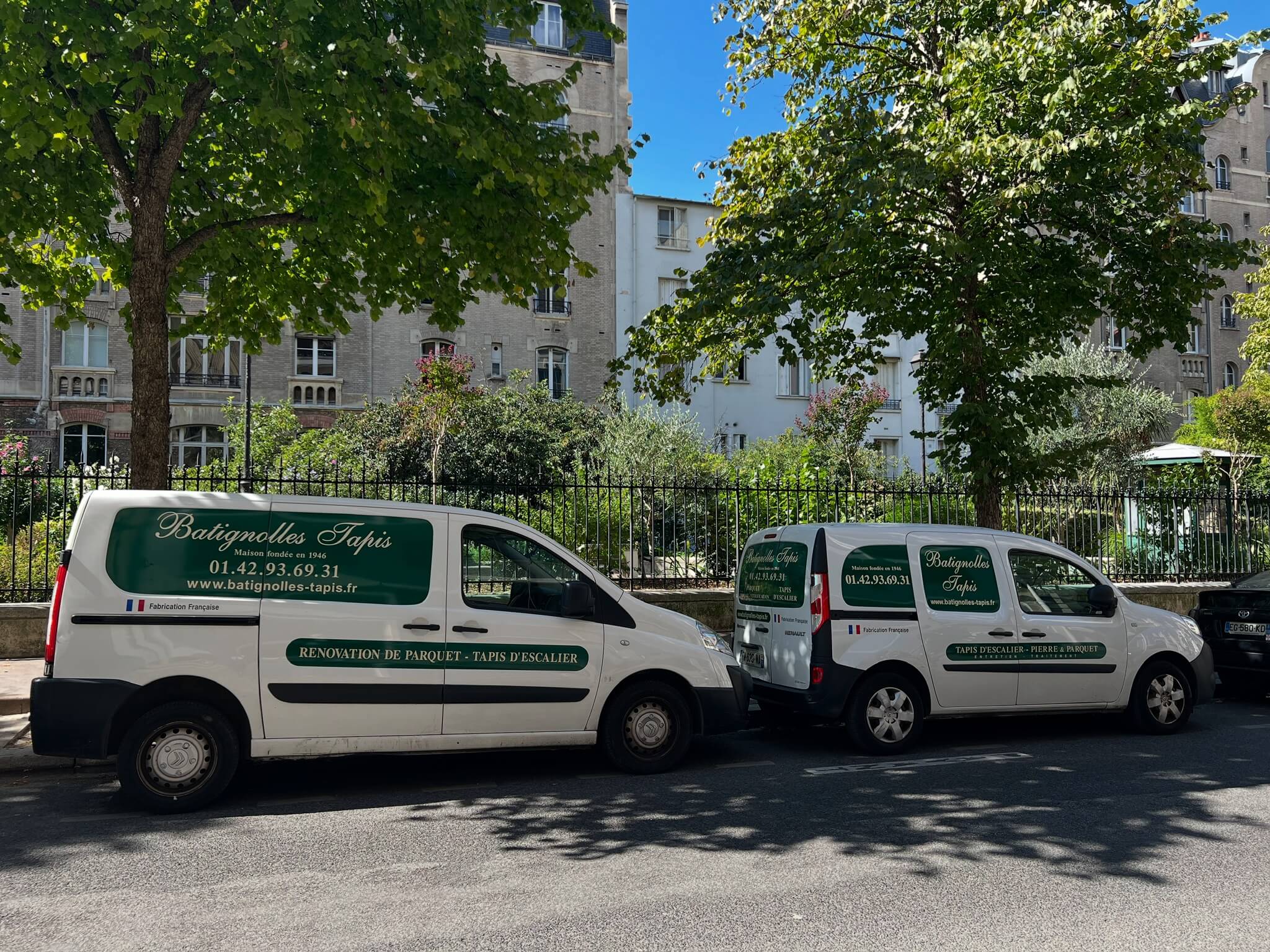 Deux camionnettes blanches Batignolles Tapis stationnées sous arbres le long d'une rue avec bâtiments en arrière-plan.