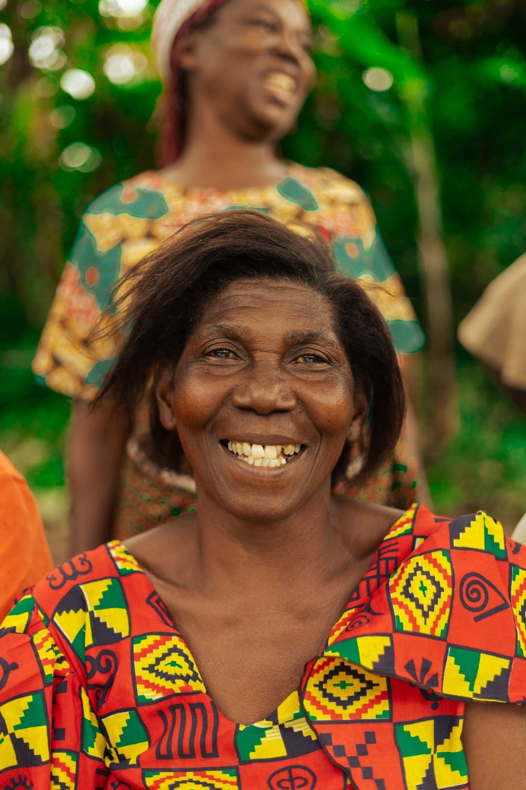 Smiling woman in colorful dress and headscarf squats beside stacked baskets full of small fish.