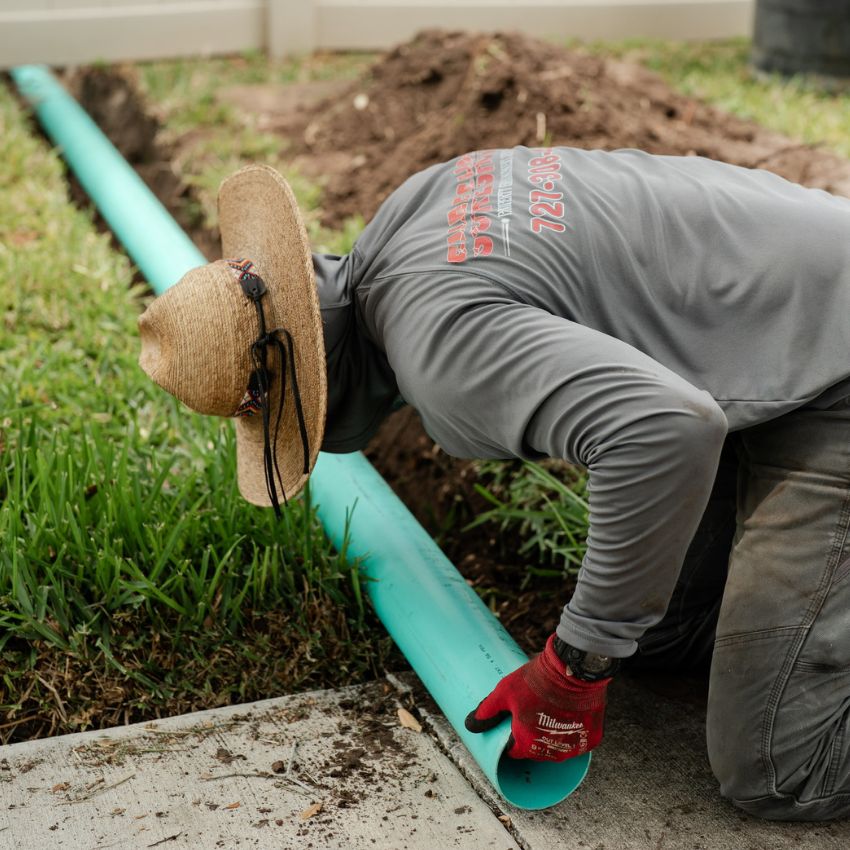 Sure Shot team member installing green drainage pipe along the edge of a lawn.