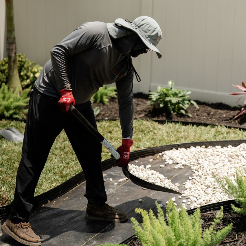 Team member spreading white decorative stone along a landscaped walkway.