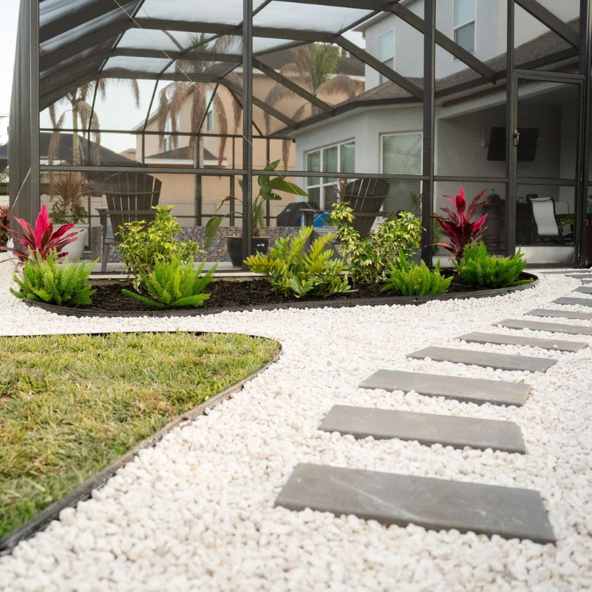 Completed backyard landscape with tropical plantings, white decorative stone, and a stepping-stone path around a screened patio.