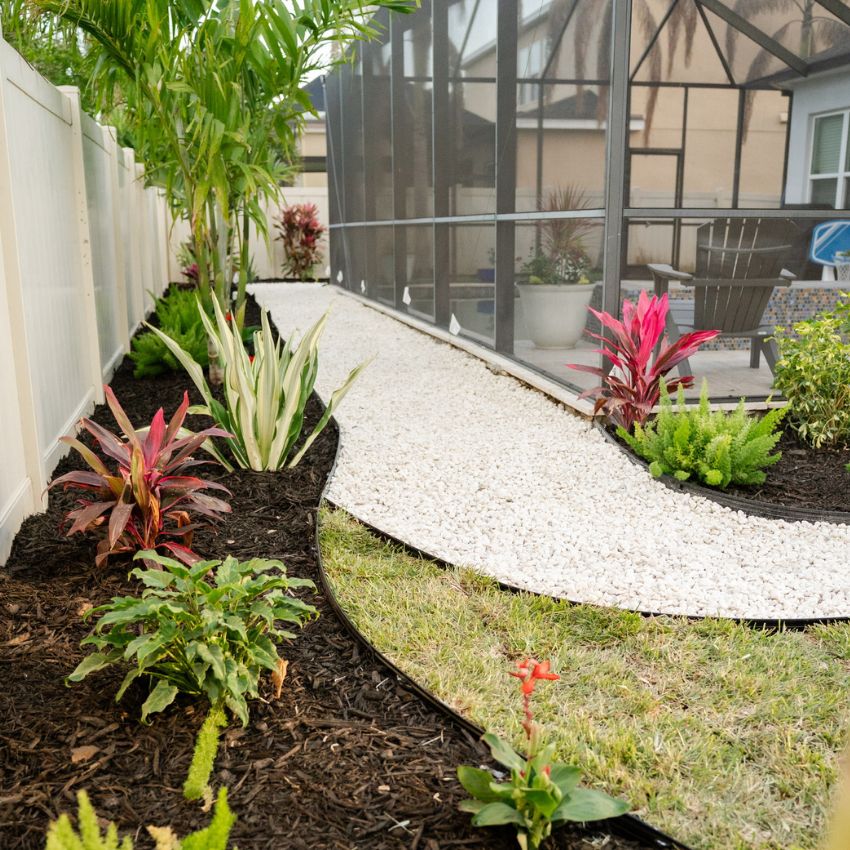 Finished side-yard landscape with tropical plantings, dark mulch, and a white stone walkway.