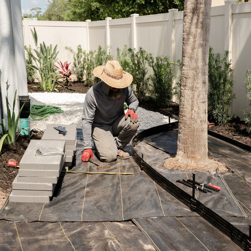 Team member installing rectangular stepping stones around a palm tree.