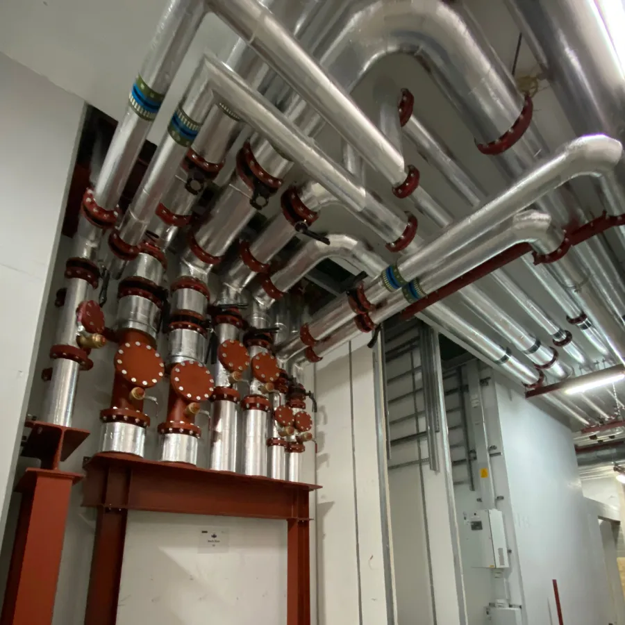 Large commercial heating pipework installation with insulated steel pipework and flanged connections in a plant room.