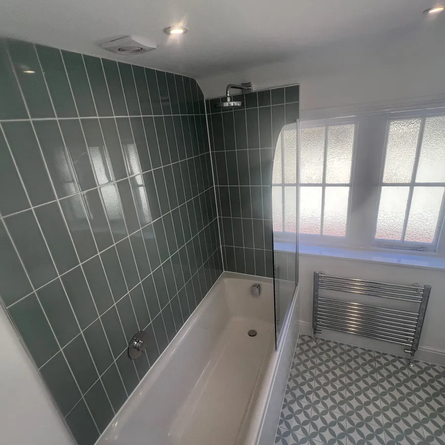 Contemporary bathroom installation with green tiled feature wall, new bath, glass shower screen and chrome towel radiator.