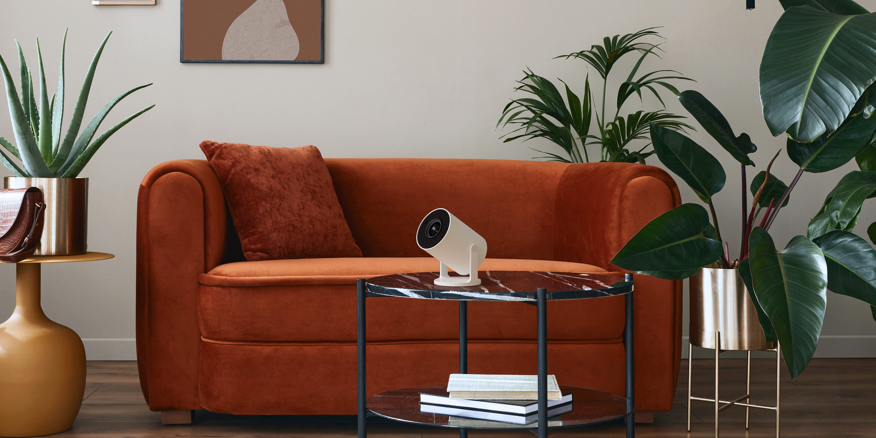 Orange velvet couch with matching pillow, side and coffee tables, houseplants, and a white smart speaker.