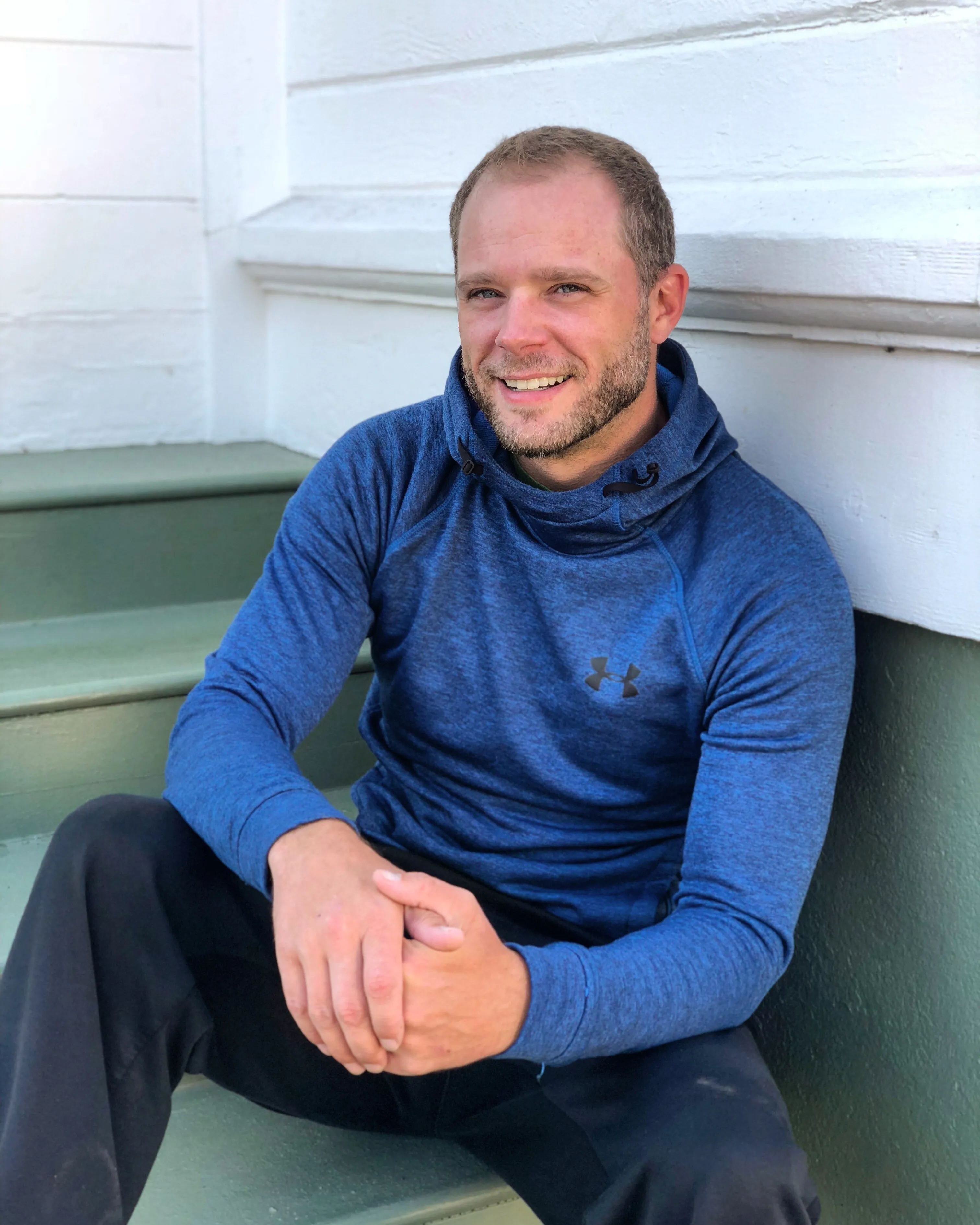 Corey Galusha, online fitness coach for busy adults, seated on a porch step