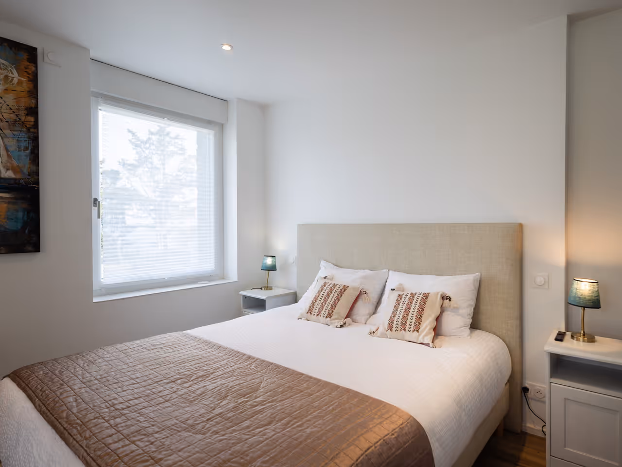 Chambre moderne avec lit double, linge blanc, coussins décoratifs et lampes sur tables de chevet.