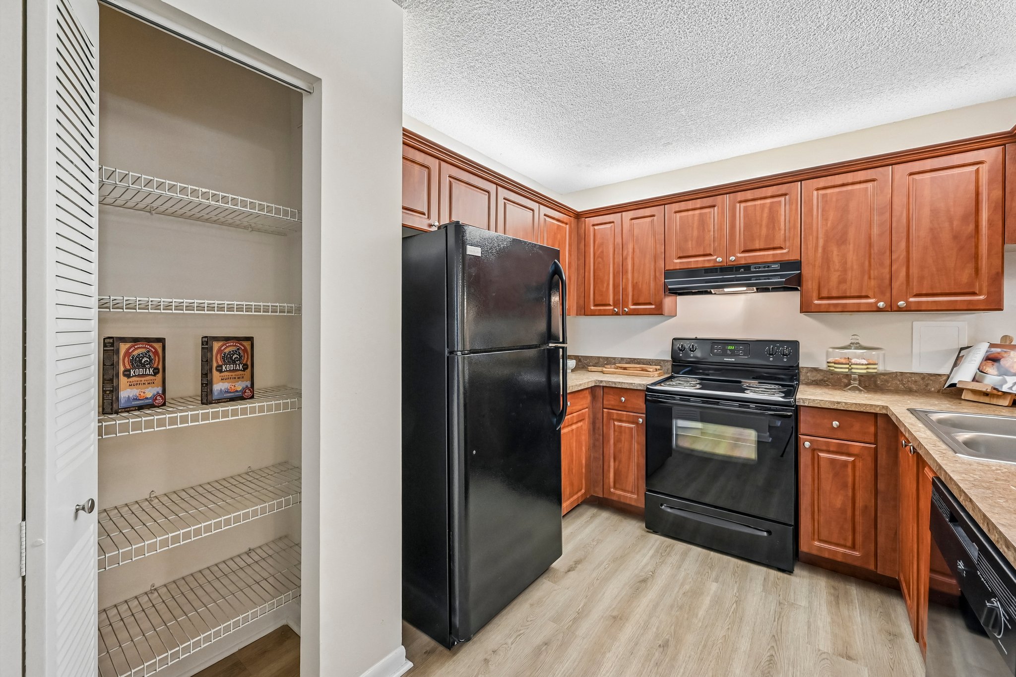 Kitchen with brown cabinets and black appliances, and empty pantry Azalea Village
