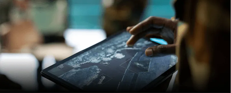 Person interacting with a tablet displaying a digital map of Earth with highlighted areas.