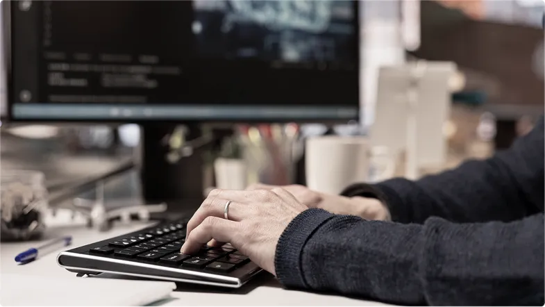 Person typing on a keyboard with a computer screen and office items in the background.
